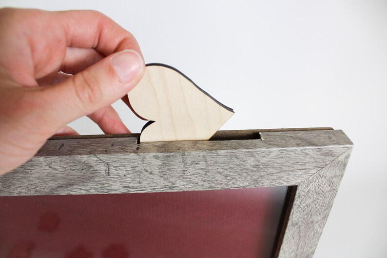 Op de afbeelding: Een houten fotolijst met een grijze verweerde afwerking. Een klein houten hartje wordt in een gleuf aan de bovenkant van de lijst geplaatst.