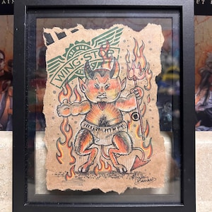May include: Framed artwork featuring a cartoon devil character with horns, a pitchfork, and flames. The artwork is on a piece of brown paper with the Wing Stop logo. The artwork is signed by Michael Barnard.