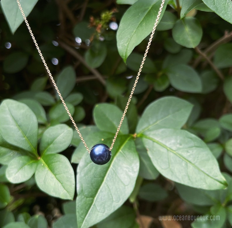 Pu&ograve; includere: Una semplice collana a catena dorata con un ciondolo a perla blu scuro.