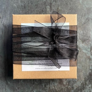 May include: A brown cardboard box with a black ribbon tied in a bow. The box has a white label with the text "Authentic Jewellery, Home and Gift Decor. Genuine Sea Glass Pearls and other Treasures. Handmade in the UK. www.oceanbounduk.com"