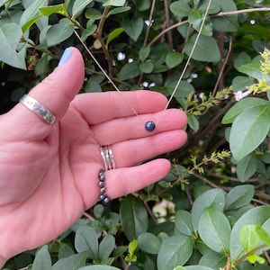 Pu&ograve; includere: Una delicata collana a catena dorata con un ciondolo di perla nera.