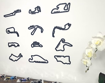 May include: A white wall with black outlines of famous race tracks, including Monaco, Valencia, and Bahrain.  The outlines are labeled with the track names.  There are several small toy race cars on a wooden table below the wall.