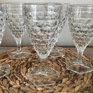 May include: A collection of clear, patterned wine glasses. The glasses have a diamond-like texture on the bowl and sit on a hexagonal base. The stems are slender, and the glasses are arranged on a woven surface.