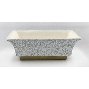 May include: A rectangular ceramic planter featuring a white interior and a speckled grey and white exterior finish. The base of the planter is a solid tan colour, and the sides flare outward towards the top rim, creating a wide, open basin shape.
