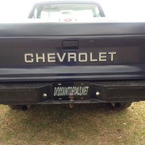 Op de afbeelding: Achteraanzicht van een donkerblauwe Chevrolet pick-up truck. Het woord "CHEVROLET" staat in zilveren letters op de achterklep. Een zwarte bumper en kentekenplaat met de tekst "DISCOUNTDECAL.NET" zijn zichtbaar.