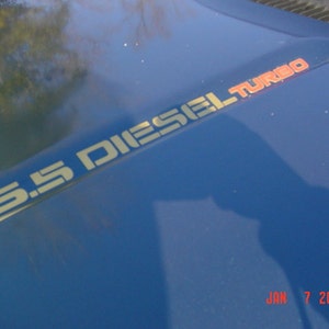 May include: A close-up of a blue vehicle hood with the text "6.5 DIESEL TURBO" in gold and red lettering. The date "JAN 7 2006" is printed in red at the bottom of the hood.