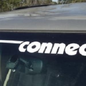 Puede incluir: Una calcomanía de vinilo blanco en el parabrisas de un vehículo. La calcomanía dice "direct connection" en una fuente estilizada. La palabra "direct" está en una fuente de escritura y la palabra "connection" está en una fuente sans-serif.