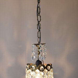 May include: A small, crystal chandelier with a brass finish and a black chain. The chandelier has a round, tiered design with multiple crystal drops.