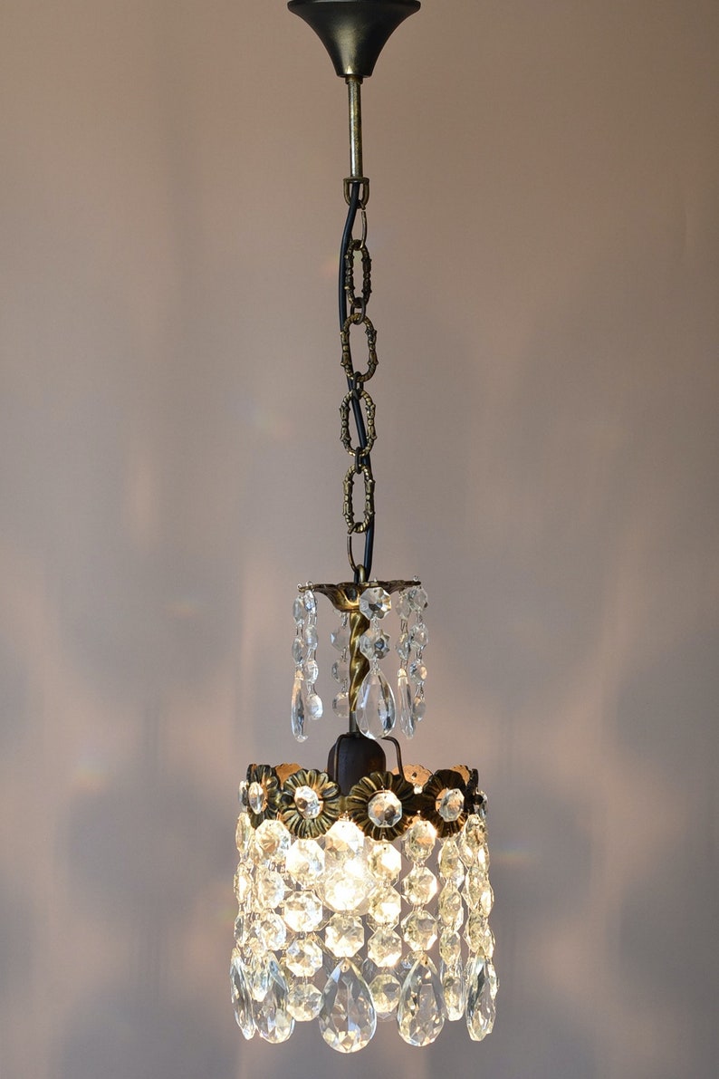 May include: A small, crystal chandelier with a brass finish and a black chain. The chandelier has a round, tiered design with multiple crystal drops.