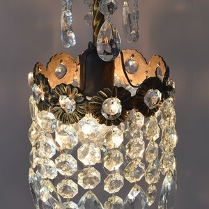 May include: A small, antique chandelier with a gold-toned metal frame and clear crystal drops. The chandelier has a round, tiered design with multiple rows of crystal drops.