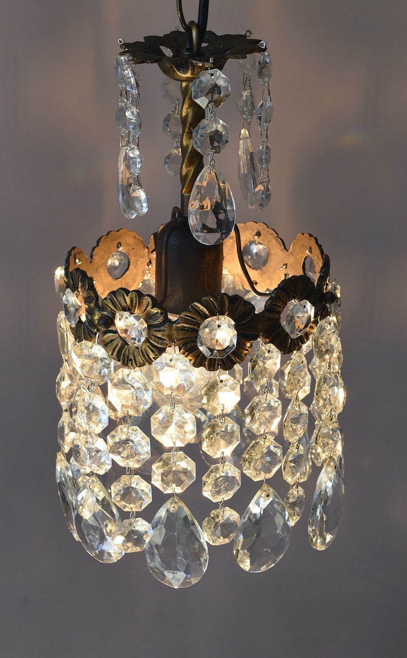 May include: A small, antique chandelier with a gold-toned metal frame and clear crystal drops. The chandelier has a round, tiered design with multiple rows of crystal drops.