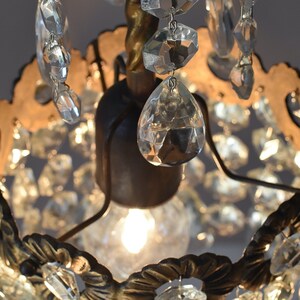 May include: A small, ornate chandelier with a gold-toned metal frame and clear crystal accents. The chandelier has a single light bulb in the center and is surrounded by a ring of crystals.