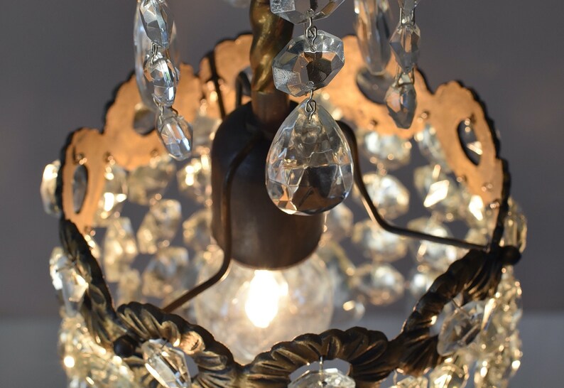 May include: A small, ornate chandelier with a gold-toned metal frame and clear crystal accents. The chandelier has a single light bulb in the center and is surrounded by a ring of crystals.