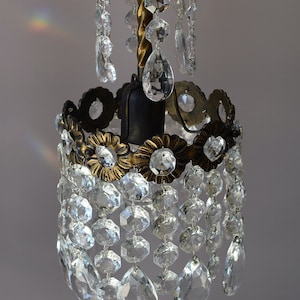 May include: A small, antique brass chandelier with crystal drops. The chandelier has a round, ornate base with a central light bulb and a chain for hanging.