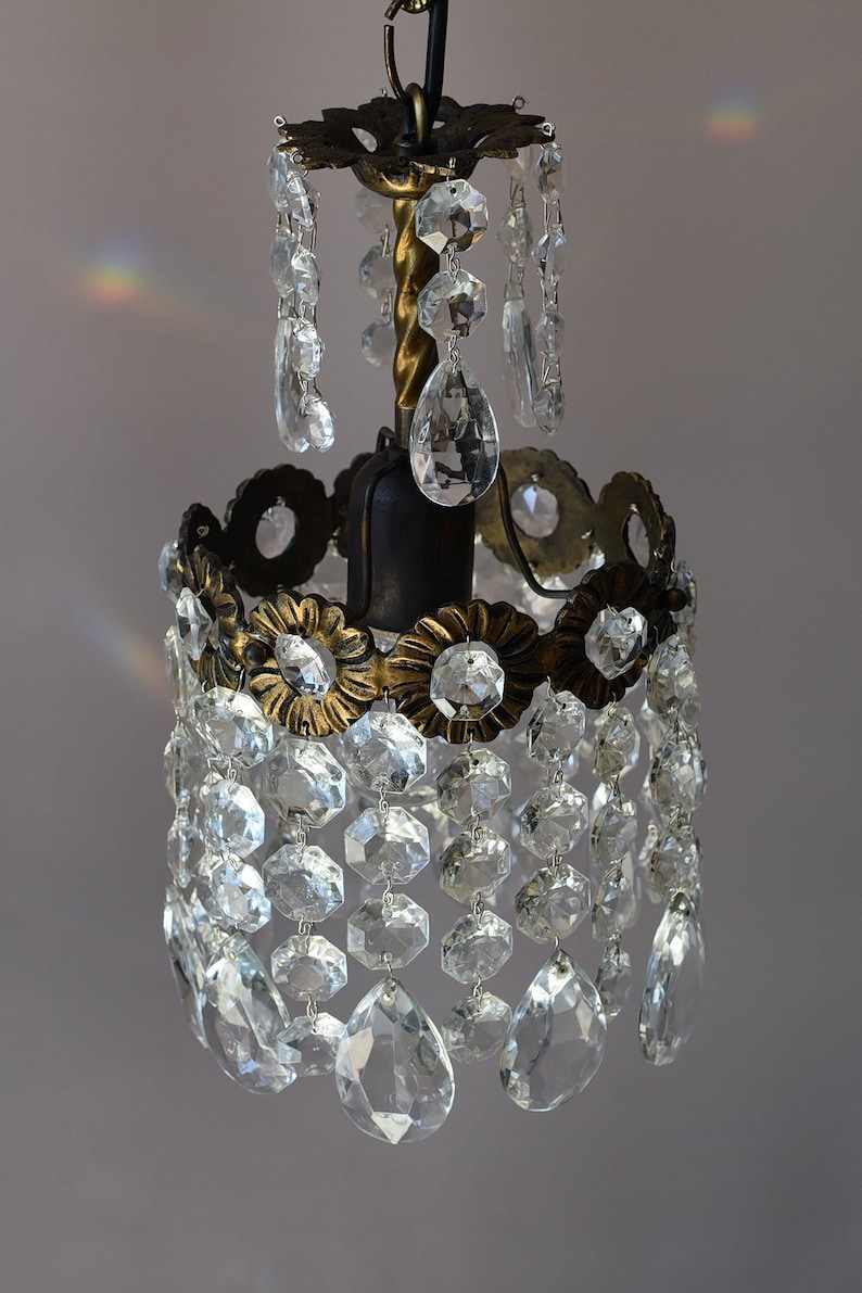 May include: A small, antique brass chandelier with crystal drops. The chandelier has a round, ornate base with a central light bulb and a chain for hanging.