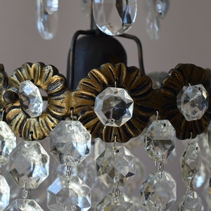 May include: A close-up of a crystal chandelier with a gold metal frame and clear glass crystals. The chandelier has a tiered design with multiple rows of crystals.