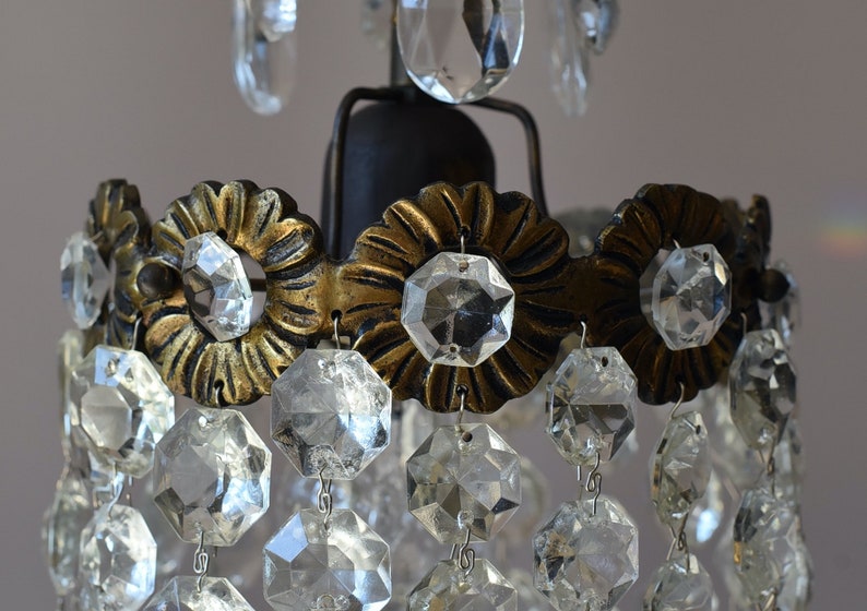 May include: A close-up of a crystal chandelier with a gold metal frame and clear glass crystals. The chandelier has a tiered design with multiple rows of crystals.