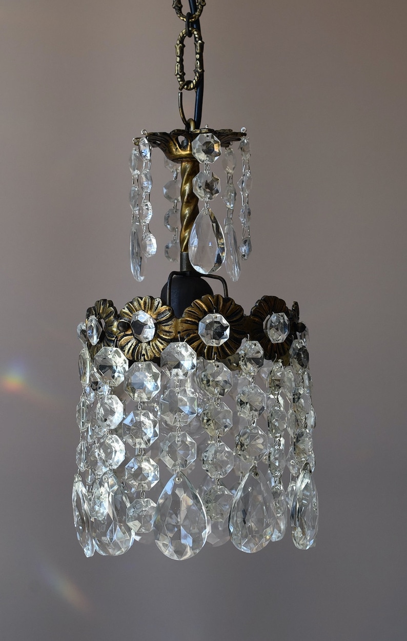 May include: A small, ornate chandelier with a gold-toned metal frame and crystal drops. The chandelier has a chain for hanging and a twisted metal rod in the center.
