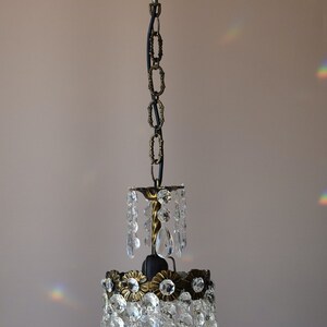 May include: A crystal chandelier with a black chain and a brass frame. The chandelier has a teardrop shape and is made of clear glass crystals.