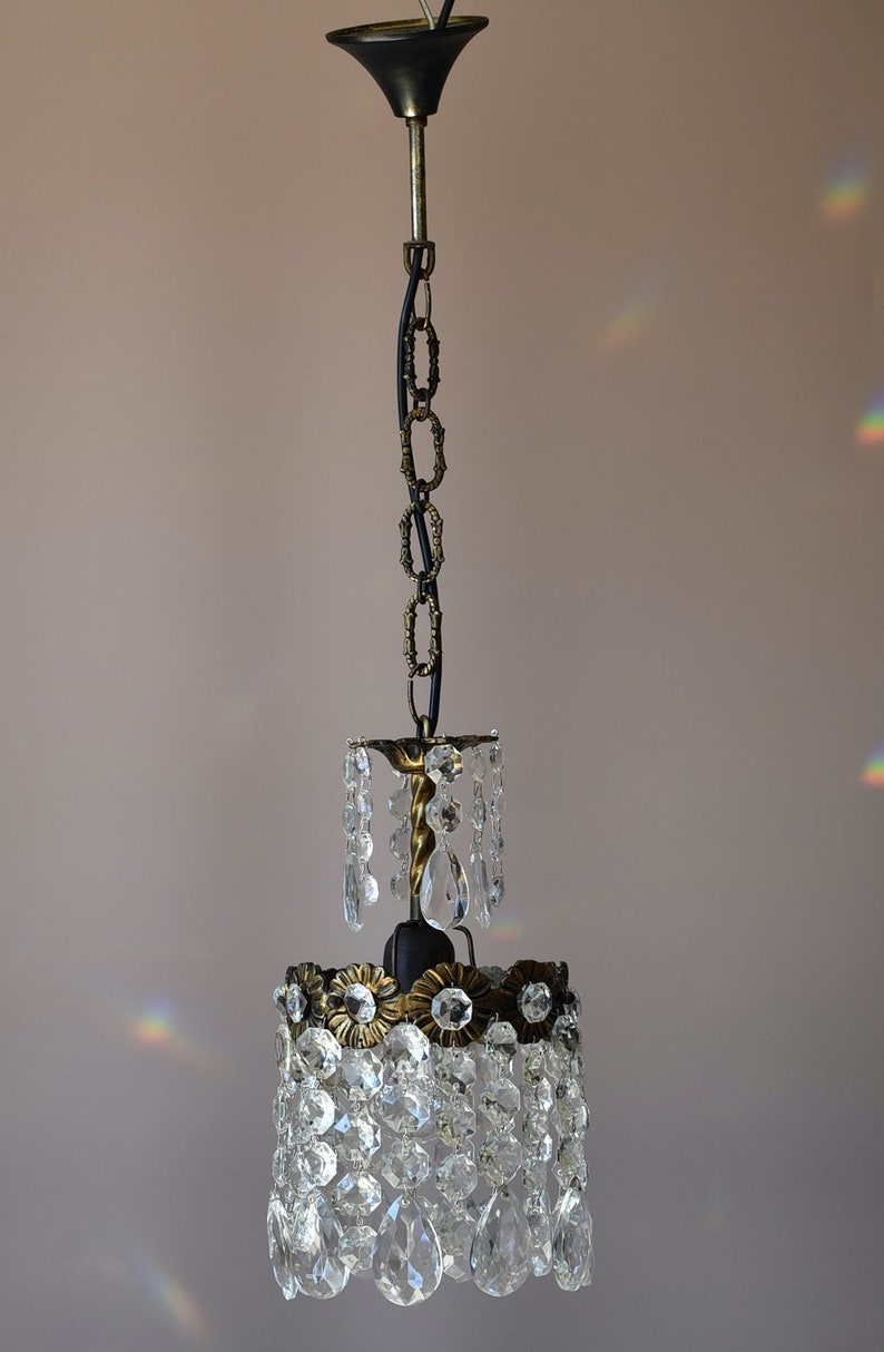 May include: A crystal chandelier with a black chain and a brass frame. The chandelier has a teardrop shape and is made of clear glass crystals.