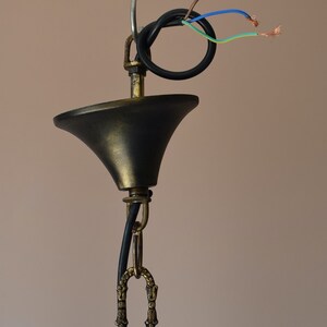 May include: Close-up of a black and gold ceiling fixture with a chain and wires. The wires are exposed and ready to be connected to an electrical outlet.