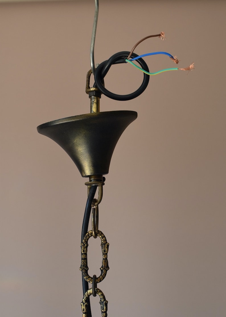 May include: Close-up of a black and gold ceiling fixture with a chain and wires. The wires are exposed and ready to be connected to an electrical outlet.
