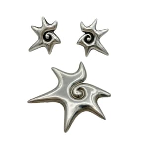 Könnte beinhalten: Ein Set silberner sternförmiger Ohrringe und eine passende Halskette mit Anhänger. Jedes Stück hat ein Spiralmuster in der Mitte.