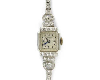 May include: A vintage Glendora wristwatch with a square face and diamond-encrusted band. The watch face has Roman numeral hour markers and a blue hand.
