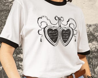 May include: White t-shirt with black trim featuring a black and white graphic of two heart-shaped lockets. The lockets have the text "Whatever our souls are made of" and "His and mine are the same."