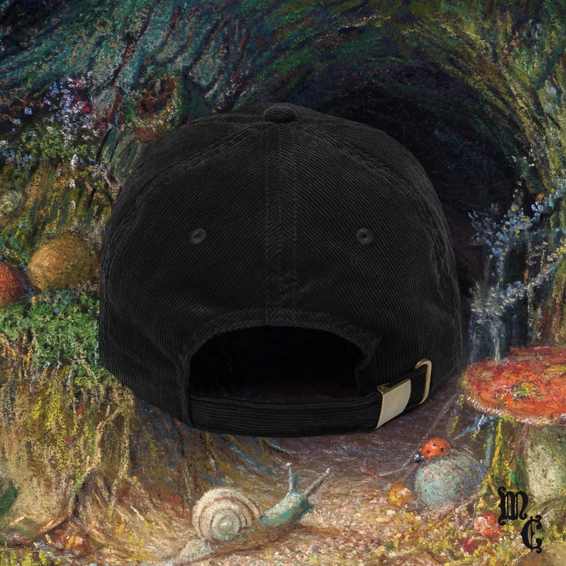 May include: Black corduroy baseball cap with a curved brim and adjustable strap. The cap features a metal buckle and a classic six-panel design. The background is a painting of a forest scene with mushrooms and a snail.