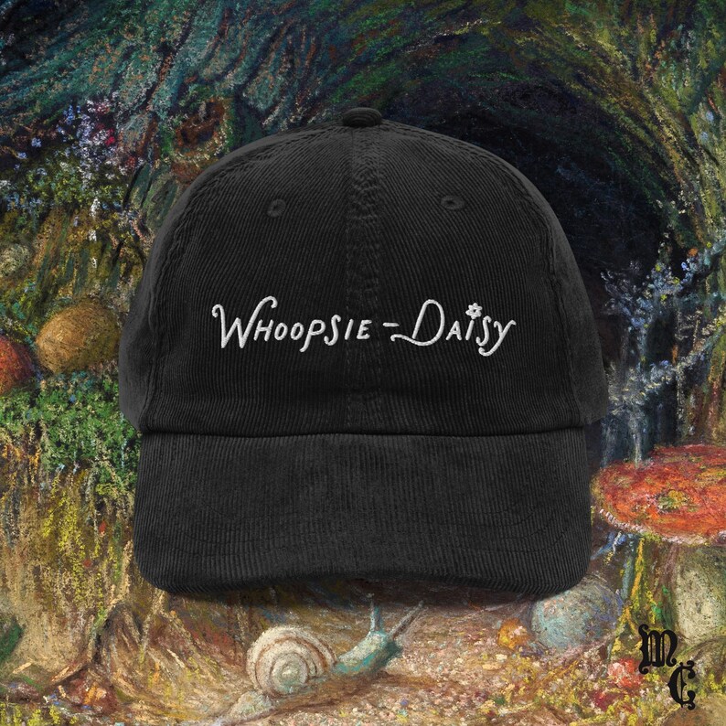 May include: Black corduroy baseball cap with the embroidered text "Whoopsie-Daisy" in white script. The cap has a curved brim and a structured crown. The background features a colorful, impressionistic painting with mushrooms and a snail.