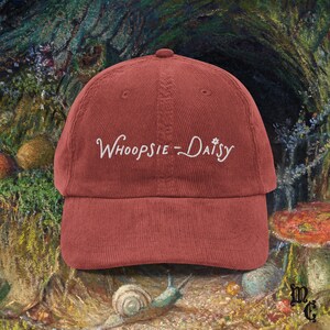 May include: A brick-red corduroy baseball cap with the embroidered text "Whoopsie-Daisy" in white script. The hat has a curved brim and a classic six-panel design, suitable for casual wear.