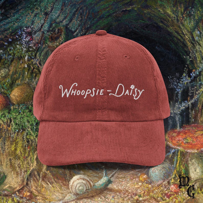 May include: A brick-red corduroy baseball cap with the embroidered text "Whoopsie-Daisy" in white script. The hat has a curved brim and a classic six-panel design, suitable for casual wear.