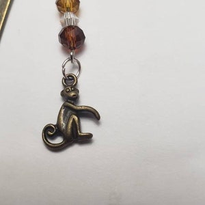 May include: A bronze bookmark with a monkey charm and a string of clear, amber, and brown glass beads.