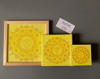 May include: Three yellow canvas paintings with a mandala design and a symbol in the center. The paintings are framed in wood and are different sizes. The largest painting is in a wooden frame.