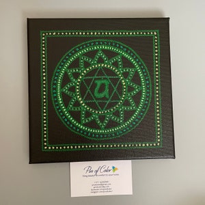 May include: A green and black canvas painting with a green mandala design. The mandala features a star with a letter "A" in the center. The painting is framed with a black border.