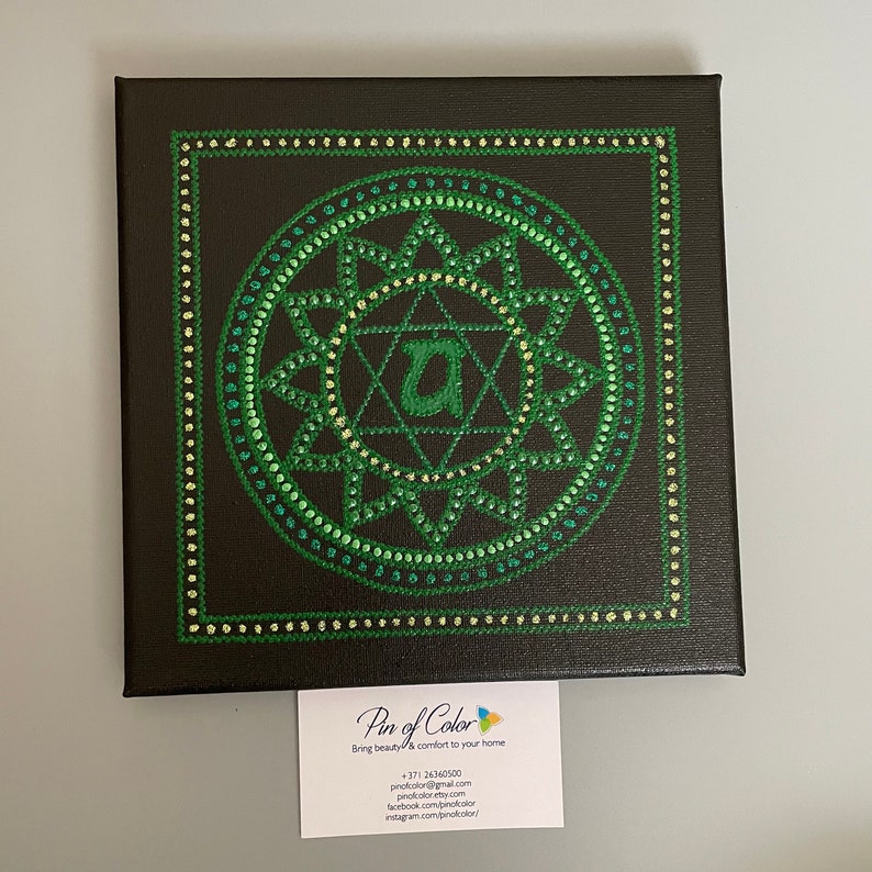May include: A green and black canvas painting with a green mandala design. The mandala features a star with a letter "A" in the center. The painting is framed with a black border.