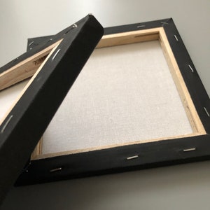 May include: Two black canvas frames with wooden stretcher bars and staples holding the canvas in place. The frames are empty and ready for painting.