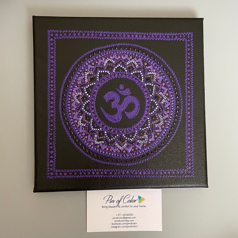 May include: Purple and white mandala with the Om symbol in the center, painted on a black canvas. The canvas is framed with a purple border.