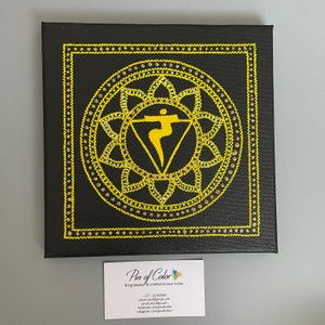 May include: A black canvas painting with a yellow mandala design. The mandala features a yellow triangle with a yellow figure inside. The painting is surrounded by a yellow border.