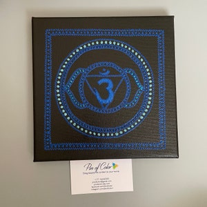 May include: A blue and teal mandala with the number 3 in the center, painted on a black canvas. The mandala is surrounded by a blue border.