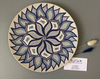 May include: A white ceramic plate with a blue and purple mandala design painted on it. The mandala is made up of dots and swirls. The plate is 12 inches in diameter.