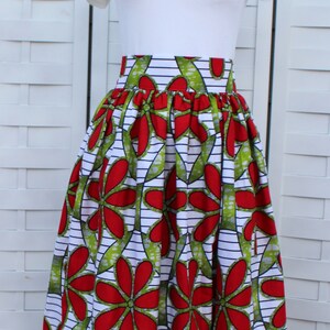 Peut inclure: Longue jupe ample avec un motif floral vibrant. La jupe pr&eacute;sente de grandes fleurs rouges avec des accents verts sur un fond blanc avec des rayures noires. Elle est associ&eacute;e &agrave; un t-shirt blanc.