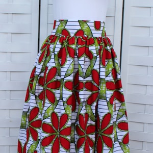 Peut inclure: Longue jupe ample avec un motif floral vibrant. La jupe pr&eacute;sente de grandes fleurs rouges avec des accents verts sur un fond blanc avec des rayures noires. Elle est associ&eacute;e &agrave; un t-shirt blanc.