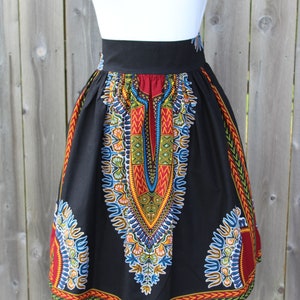 May include: Black skirt with a vibrant, colorful African print. The skirt features a high waist and a knee-length hem. The print includes red, yellow, blue, and green geometric patterns. The skirt is displayed on a white mannequin.