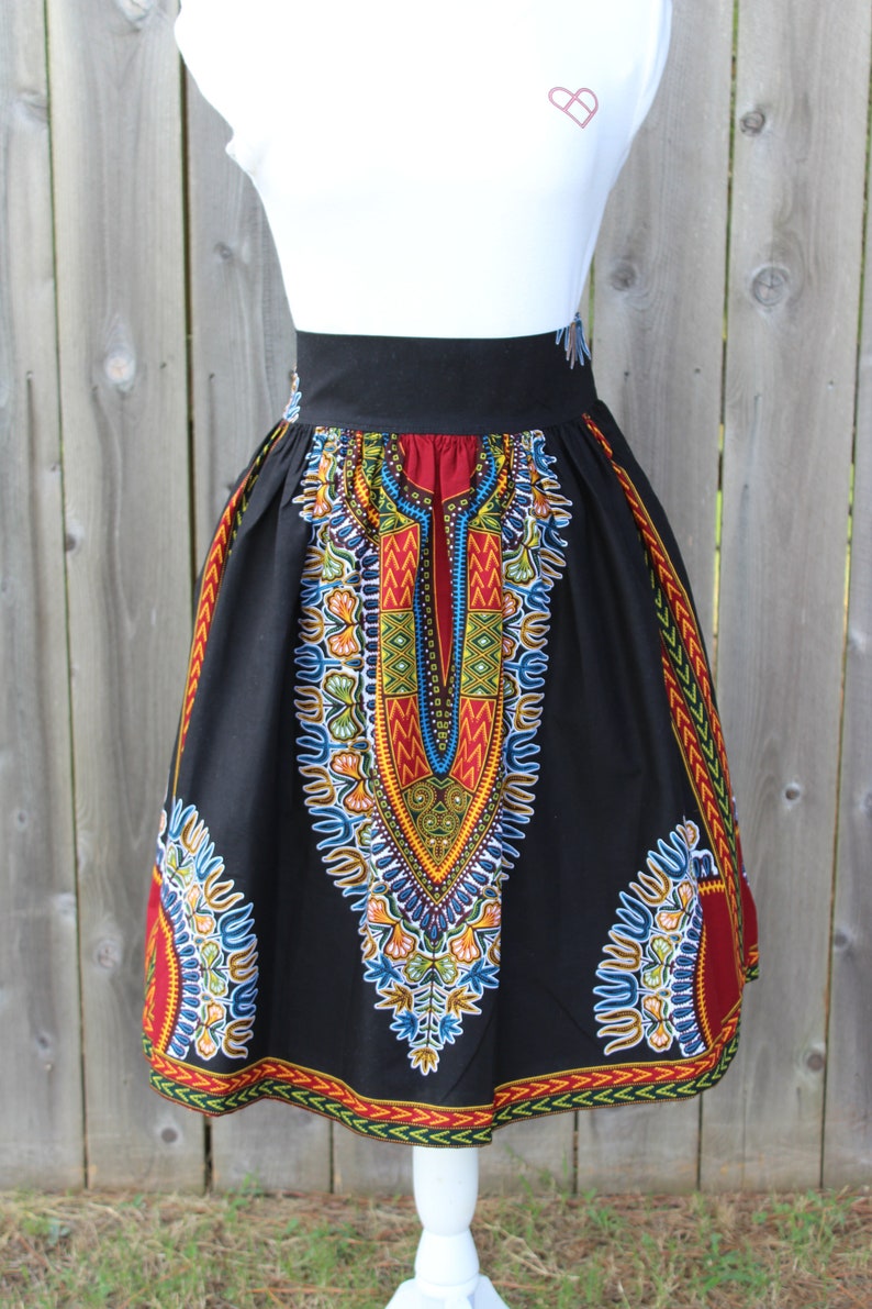 May include: Black skirt with a vibrant, colorful African print. The skirt features a high waist and a knee-length hem. The print includes red, yellow, blue, and green geometric patterns. The skirt is displayed on a white mannequin.