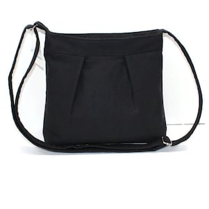 May include: A black crossbody bag with a rectangular shape and a long, adjustable strap. The bag features a pleated design on the front and a simple, minimalist aesthetic. The strap is thin and made of the same material as the bag.