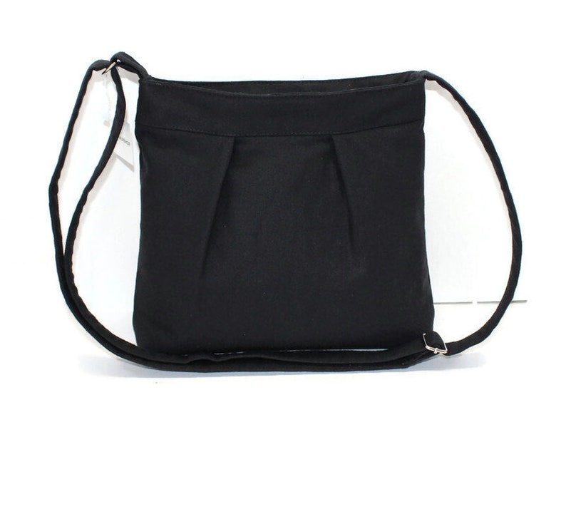 May include: A black crossbody bag with a rectangular shape and a long, adjustable strap. The bag features a pleated design on the front and a simple, minimalist aesthetic. The strap is thin and made of the same material as the bag.