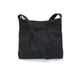 May include: A black shoulder bag with a long strap. The bag is made of a solid black fabric and features a pleated design on the front. The strap is attached to the top corners of the bag.