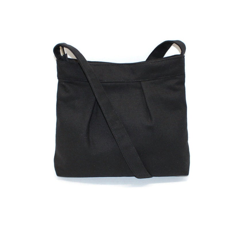 May include: A black shoulder bag with a long strap. The bag is made of a solid black fabric and features a pleated design on the front. The strap is attached to the top corners of the bag.